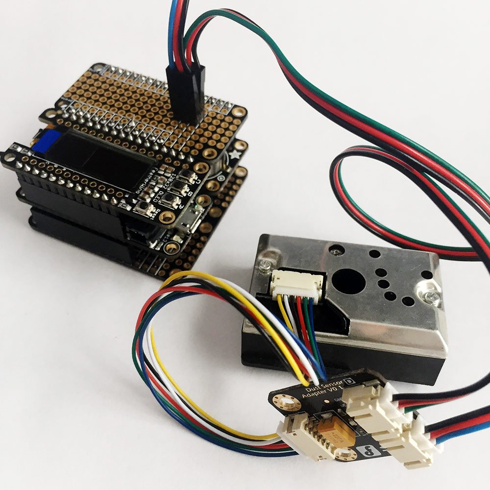A SensorGrid node on the bench: the stacked Feather boards with their OLED, the particulate sensor, and the dust sensor adapter board wired between them